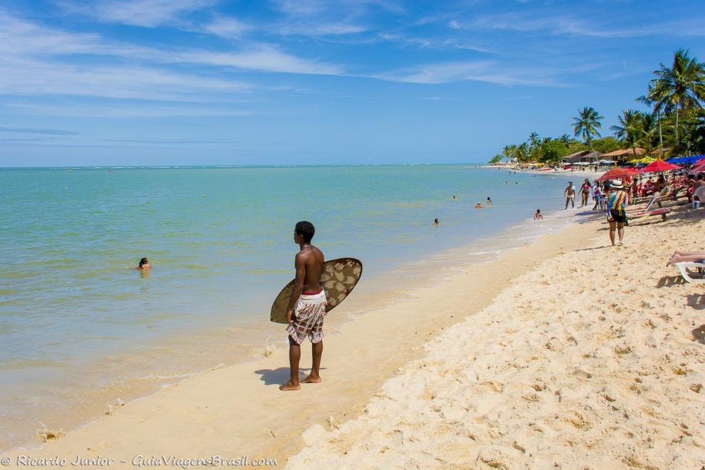 Imagem de um menino segurando sua prancha e admirando o mar da Praia do Mutá.